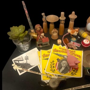 May include: A collection of miniature wooden figurines, a small metal bucket with a green plant, and several yellow and red "Handmade American Citizen" labels with a portrait of George Washington. Other items include a small house, a monkey figurine, and a playing card.