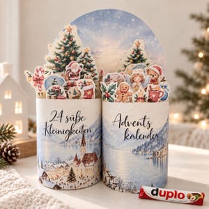 Könnte beinhalten: Ein zylindrischer Adventskalender mit einer winterlichen Landschaft, einem verschneiten Dorf und einem See. Auf der Vorderseite steht der Text 24 süße Kleinigkeiten und Advents kalender. Oben sind Aufsteller mit Weihnachtsbäumen, dem Weihnachtsmann und Leckereien.