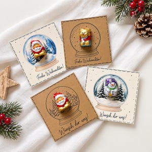 Könnte beinhalten: Vier quadratische Karten mit Illustrationen von Schneekugeln und befestigten Schokoladenfiguren. Zwei Karten zeigen den Weihnachtsmann, eine einen Bären und eine einen Schneemann. Text: Frohe Weihnachten und Wünsch dir was.