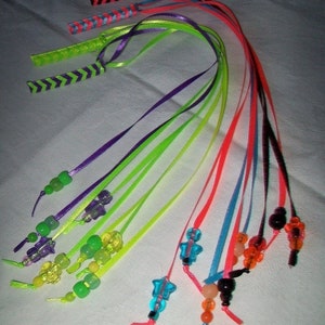 May include: A collection of colorful hair accessories featuring vibrant ribbons and beaded accents. The ribbons come in various shades, including neon green, purple, red, and blue. Some ribbons have decorative woven patterns. The beaded accents include star and round shapes.