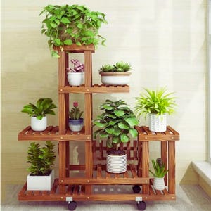 Könnte beinhalten: Ein mehrstöckiger Pflanzenständer aus Holz mit verschiedenen Topfpflanzen. Der Ständer ist in einem warmen Braunton gehalten und verfügt über mehrere Regale unterschiedlicher Größe. Die Pflanzen umfassen grünes Laub und blühende Pflanzen in weißen, blauen und gestreiften Töpfen. Der Ständer hat Räder.
