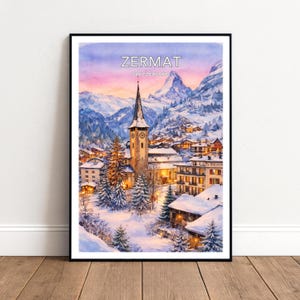 May include: A framed watercolour print depicting Zermatt, Switzerland. The image shows a snow-covered village in the Swiss Alps, with a church steeple, lit buildings, and snow-covered fir trees under a twilight sky.