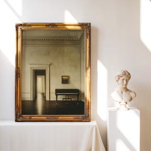 May include: A framed artwork with a gold ornate frame, depicting a room with a piano and a painting. A marble bust of a woman sits on a white pedestal. The artwork is on a white tablecloth.