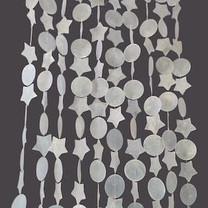 May include: A decorative hanging curtain composed of multiple vertical strands featuring alternating white, iridescent, circular and star-shaped shell pieces. Each individual shell component is connected by thin, clear thread, creating a shimmering, translucent, and layered visual effect throughout the entire length of the hanging display.
