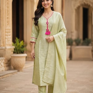 May include: A light green three-piece outfit consisting of a long-sleeved straight-cut tunic with a pink trim and tassel detail at the neckline, matching straight-leg trousers, and a coordinating lightweight shawl draped over one shoulder.