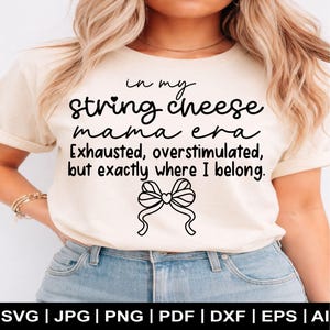 Könnte beinhalten: Cremefarbenes T-Shirt mit dem Text "in my string cheese mama era Exhausted, overstimulated, but exactly where I belong." Eine schwarze Schleife befindet sich unter dem Text. Dateityp-Optionen werden unten angezeigt.
