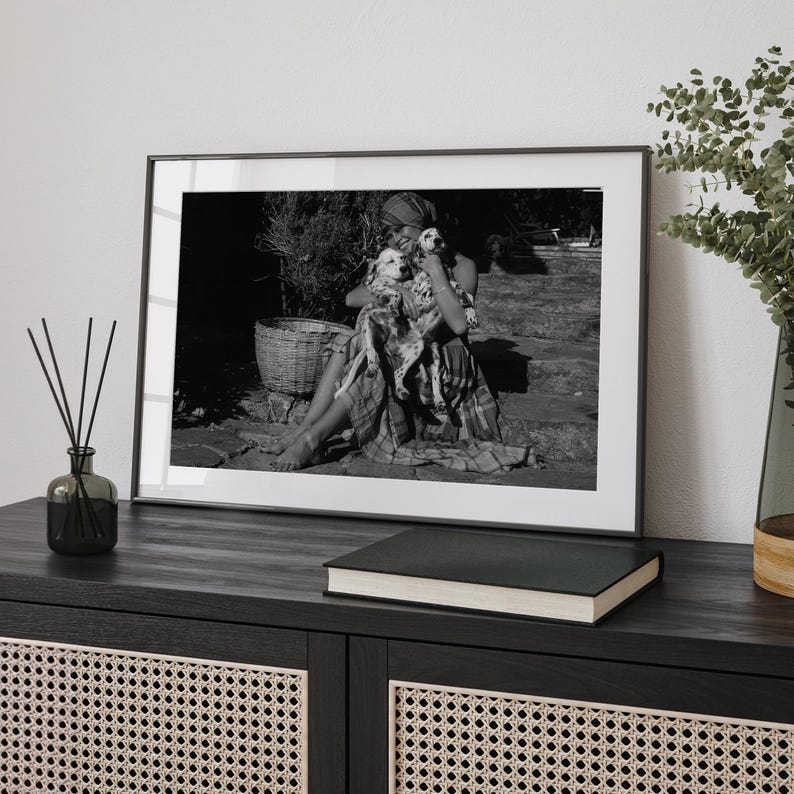 A framed black and white photograph of a woman sitting on a bench, holding a dog, is displayed on a wooden cabinet.