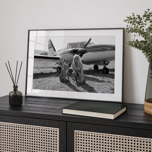 A framed black and white photograph of a woman and a cat, with a small airplane in the background, is displayed on a wooden cabinet.