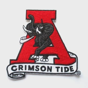 Könnte beinhalten: Gestickter Aufnäher mit einem roten "A" und einem schwarzen Elefanten-Maskottchen. Der Aufnäher enthält den Text "CRIMSON TIDE" auf einem weißen Banner, mit einem Nike-Logo. Der Aufnäher befindet sich auf weißem Hintergrund.