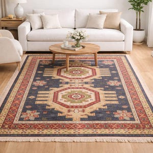 Puede incluir: Una alfombra rectangular con un campo azul marino y un diseño geométrico central en beige, rojo y verde. La alfombra tiene un borde estampado y un borde con flecos, adecuada para una sala de estar, con medidas en cm.