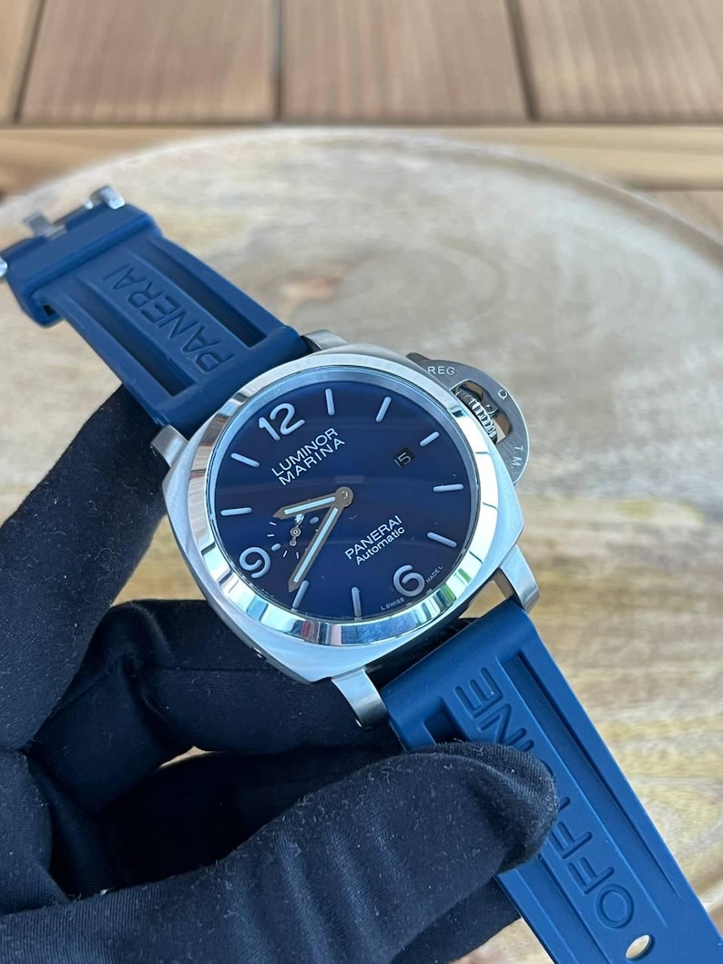 May include: A stainless steel Panerai Luminor Marina Automatic watch with a blue dial and blue rubber strap. The watch face displays the time with luminous hands and markers. The strap is marked with the Panerai logo.