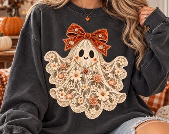 Könnte beinhalten: Ein anthrazitfarbenes Sweatshirt mit Rundhalsausschnitt und einem zentralen Grafikdruck eines Geistes, der mit cremefarbenen Spitzenmustern, kleinen orangefarbenen Kürbissen und Blumen verziert ist. Der Geist trägt eine große rostrote Samtschleife.