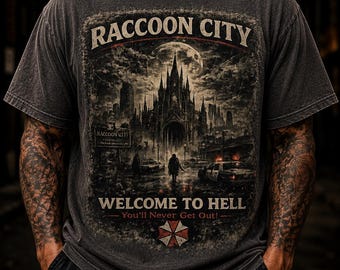 Könnte beinhalten: Ein anthrazitfarbenes Kurzarm-T-Shirt mit einem Grafikdruck einer gotischen Skyline unter einem Vollmond. Der Text lautet RACCOON CITY, WELCOME TO HELL und You'll Never Get Out, mit einem rot-weißen regenschirmförmigen Logo am unteren Rand.