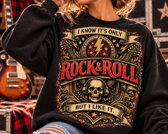 Könnte beinhalten: Ein schwarzes Langarm-Sweatshirt mit einem Grafikdruck, der einen Totenkopf mit Kopfhörern, einen Blitz und den Text "I KNOW IT'S ONLY ROCK & ROLL BUT I LIKE IT" zeigt. Das Design enthält verzierte goldene Schnörkel und rote Akzente.
