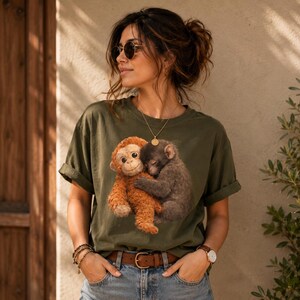 Viral lonely monkey Comfort Colors shirt featuring a baby monkey hugging a stuffed toy, modeled by a stylish couple wearing matching oversized graphic tees in pepper and ivory colors.