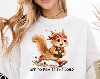 Könnte beinhalten: Ein weißes Langarm-Sweatshirt mit einer Grafik eines Cartoon-Eichhörnchens, das ein rotes gepunktetes Bandana und rote Turnschuhe trägt und ein braunes Buch mit einem goldenen Kreuz hält. Der Text darunter lautet OFF TO PRAISE THE LORD.