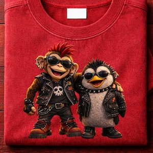 Puede incluir: Camiseta roja con un mono y un pingüino de dibujos animados, ambos con gafas de sol y chaquetas de cuero. El mono tiene un mohawk y el pingüino un collar con tachuelas. La camiseta está doblada, sin texto visible.