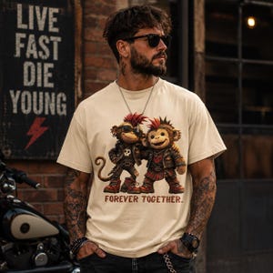 May include: A beige short-sleeve t-shirt featuring a graphic of two monkeys with mohawks, leather jackets, and boots. The monkeys are standing side by side with arms around each other. Below the graphic, the text reads "FOREVER TOGETHER..." in a brown, distressed font.
