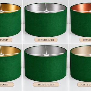 May include: Six cylindrical lampshades with a dark green exterior fabric. The interiors feature metallic finishes labelled as Brush Gold, Brush Silver, Brush Copper, Matte Gold, Matte Silver, and Matte Champagne, each with a white spider fitter.