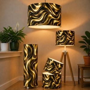 Op de afbeelding: Een collectie cilindrische lampenkappen en een driepootvloerlamp met een zwart en goud golvend, vloeistofachtig patroon. De set bevat een grote hangende kap, een hoge vloercilinder, twee kleinere kappen en een driepootlamp.