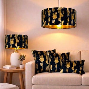 Peut inclure: Un salon moderne avec un abat-jour et des coussins à motifs noirs et dorés. Une base de lampe blanche et une petite table d'appoint avec une plante et des livres sont également visibles. L'abat-jour et les coussins présentent un motif de feuilles d'or.