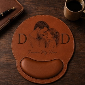 May include: Brown leather mouse pad with a wrist rest. The pad features an engraved image of a father and child, with the word "DAD" on either side of the image. The text "Forever My Hero" is below the image.