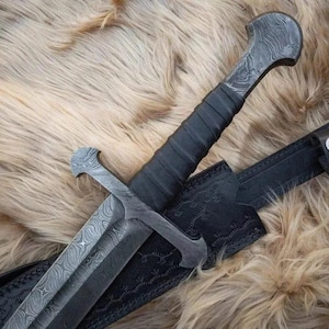 Puede incluir: Imagen detallada de una espada con una hoja estampada y un mango envuelto en cuero negro. La espada est&aacute; parcialmente enfundada en una vaina de cuero negro con costuras decorativas. El fondo es una superficie texturizada de color marr&oacute;n claro.