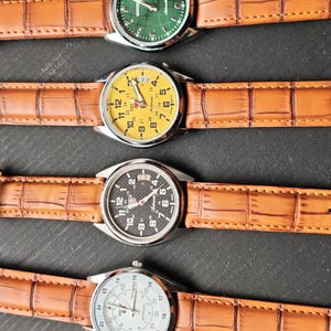 May include: Four wristwatches with brown leather straps are displayed. The watch faces are green, yellow, black, and white. The watch faces have numbers and hands. The straps have a crocodile skin pattern.