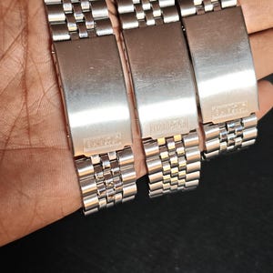 May include: Three stainless steel watch bands with a brushed finish. Each band features a rectangular clasp with the "SEIKO" brand name. The bands are composed of small, interconnected links.