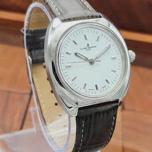 May include: A silver-toned wristwatch with a white face and black leather band. The watch features the brand name "Ulysse Nardin" and has a classic design. The band is approximately 8 inches long.