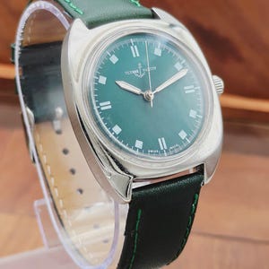 K&ouml;nnte beinhalten: Eine Vintage-Armbanduhr von Ulysse Nardin mit gr&uuml;nem Zifferblatt und silbernen Zeigern. Die Uhr hat ein Edelstahlgeh&auml;use und ein gr&uuml;nes Lederarmband mit gr&uuml;nen N&auml;hten. Auf dem Zifferblatt stehen der Markenname und "SWISS MADE".