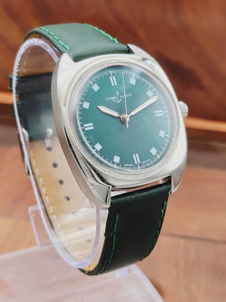 K&ouml;nnte beinhalten: Eine Vintage-Armbanduhr von Ulysse Nardin mit gr&uuml;nem Zifferblatt und silbernen Zeigern. Die Uhr hat ein Edelstahlgeh&auml;use und ein gr&uuml;nes Lederarmband mit gr&uuml;nen N&auml;hten. Auf dem Zifferblatt stehen der Markenname und "SWISS MADE".