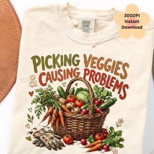 Könnte beinhalten: Cremefarbenes T-Shirt mit dem Text "PICKING VEGGIES & CAUSING PROBLEMS" über einem Weidenkorb voller Gemüse. Das Design umfasst Karotten, Tomaten, Gurken und Radieschen. Ein Paar Gartenhandschuhe befindet sich unten.