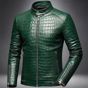 Puede incluir: Chaqueta de cuero verde con textura de piel de cocodrilo. La chaqueta tiene cuello alto, cremallera frontal y bolsillos con cremallera. Las mangas también tienen cremalleras. La chaqueta es de color verde medio.