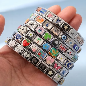 May include: A hand displays multiple stainless steel charm bracelets. Each link of the bracelets has a colourful enamel charm with diverse designs, such as a strawberry, a football, and a Union Jack.