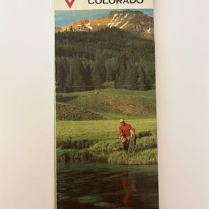 May include: A vintage Conoco Colorado travel brochure. The cover features a scenic illustration of a mountain range, a forest, and a man and child fishing in a river. The brochure is rectangular and has the Conoco logo at the top.
