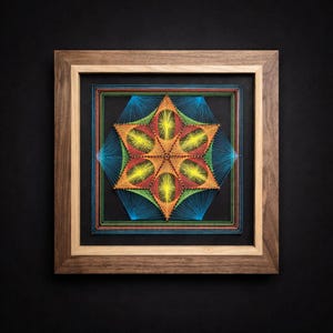 Könnte beinhalten: Ein gerahmtes String-Art-Stück mit einem sechszackigen Stern-Design. Der Stern besteht aus orangefarbenen, gelben und roten Fäden, wobei blaue Fäden die äußeren Punkte bilden. Das Kunstwerk befindet sich vor einem schwarzen Hintergrund in einem Holzrahmen.
