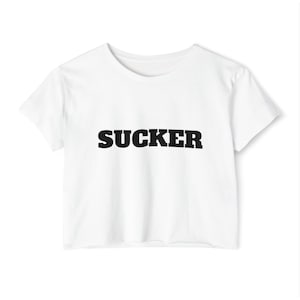 May include: White crop top t-shirt with the word "SUCKER" printed in bold, black letters across the front. The shirt has short sleeves and a crew neck. The t-shirt is made of a soft, lightweight material.