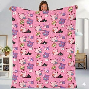 May include: A pink blanket featuring a repeating pattern of cartoon characters, flowers, and envelopes. The blanket is held up by a person. The characters are in shades of pink, purple, and black. The blanket is a soft, cozy item.
