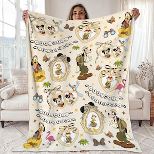 May include: A cream-colored blanket featuring various Disney characters such as Mickey and Minnie Mouse, Donald Duck, Goofy, and Pluto. The blanket has a repeating pattern of framed characters, butterflies, and the text "ANIMAL KINGDOM".