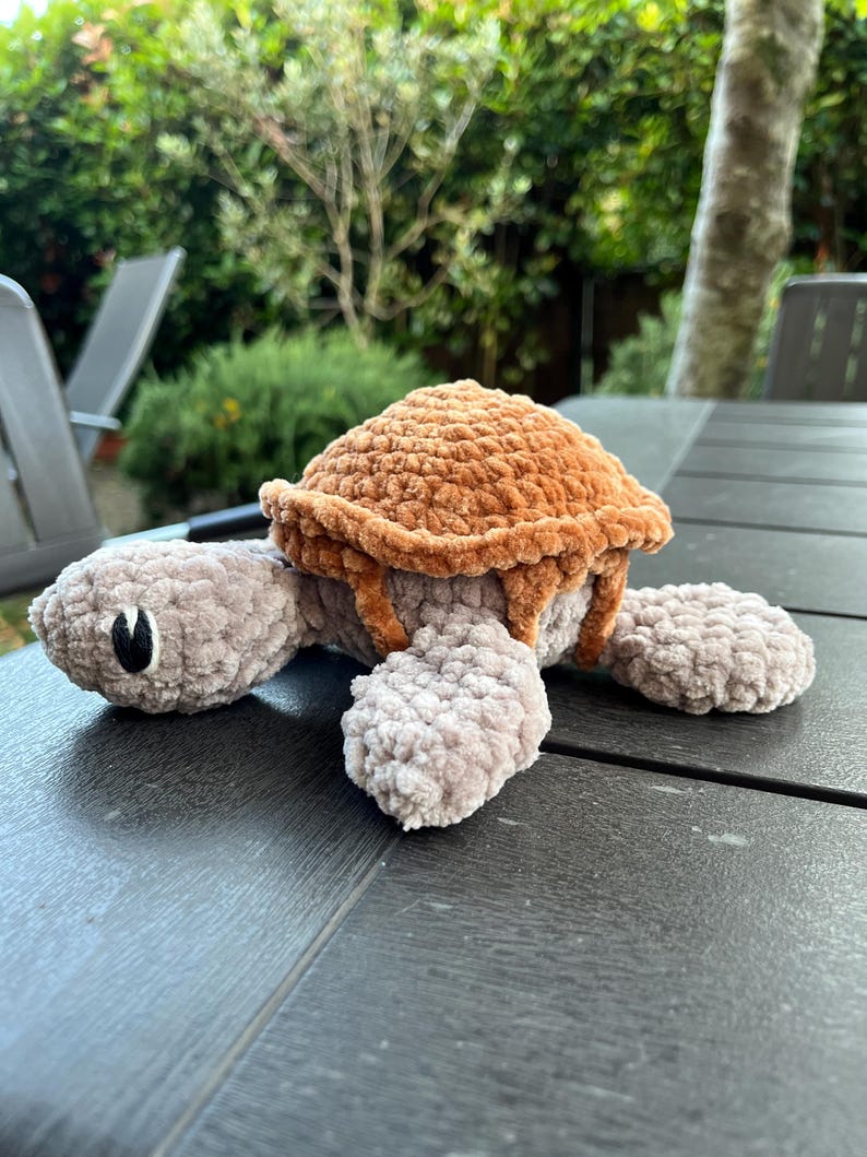 K&ouml;nnte beinhalten: Ein Pl&uuml;schschildkr&ouml;ten-Spielzeug aus weichem, strukturiertem Garn. Die Schildkr&ouml;te hat einen hellgrauen Kopf, Gliedma&szlig;en und einen Bauch, die mit einem abgerundeten, dunkelbraunen Panzer kontrastieren. Sie hat einfache schwarze Augen.