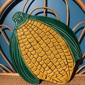 Peut inclure: Un plat de service en céramique en forme d'épi de maïs. Le plat présente un motif d'épi de maïs jaune avec des feuilles vertes. Le plat en céramique est une pièce décorative pour servir des aliments.
