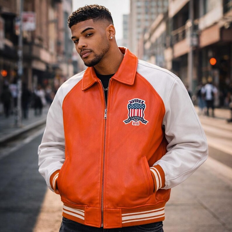 May include: Orange and white leather jacket with a zip closure and a patch on the chest. The jacket has white sleeves and a white collar. The patch features a design with the text "NVIREX" and "The American Dream 2775".