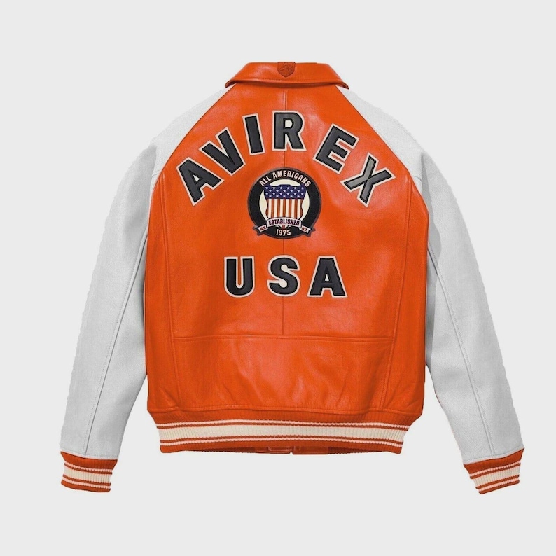 May include: Orange and white leather jacket with the text "AVIREX" and "USA" on the back. The jacket has white sleeves and a striped hem. A patch with the words "ALL AMERICANS ESTABLISHED 1975" and a US flag is centered on the back.
