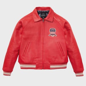 May include: A vibrant red leather jacket with a classic bomber style. Features a collared neckline, a zipper closure, and a patch on the chest. The cuffs and hem have white and red striped detailing. The jacket has a logo patch that says "AVIREX".