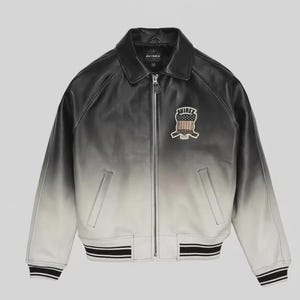 May include: A black and white gradient leather jacket with a zip-up front and a collared neckline. The jacket features a patch on the chest with a crest design and the brand name "AVIREX". The cuffs and hem have black and white striped detailing.