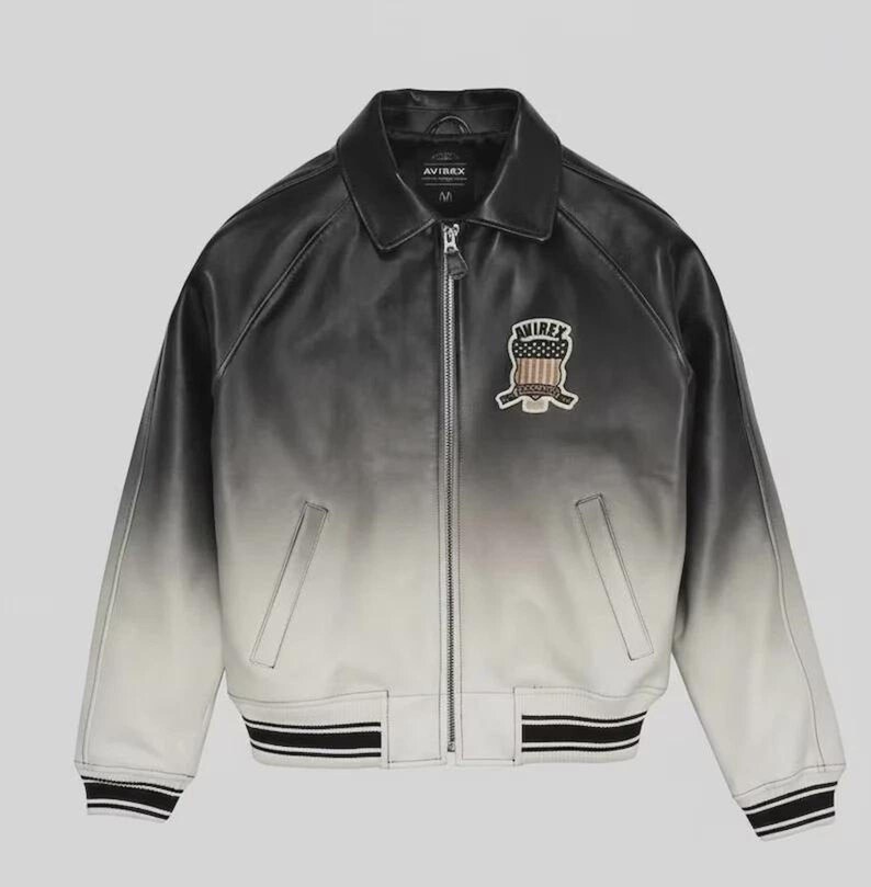 May include: A black and white gradient leather jacket with a zip-up front and a collared neckline. The jacket features a patch on the chest with a crest design and the brand name "AVIREX". The cuffs and hem have black and white striped detailing.