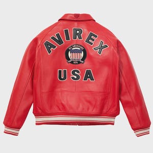 May include: Red leather jacket with the word "AVIREX" arched across the shoulders and "USA" below a circular patch with the American flag. The jacket has a ribbed collar, cuffs, and hem with white stripes. The jacket is a classic bomber style.