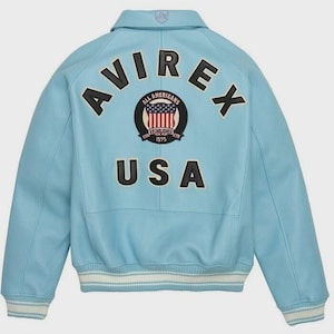 May include: A light blue leather jacket with the word "AVIREX" arched across the upper back. Below the word "AVIREX" is a circular patch with the words "ALL AMERICANS" and "ESTABLISHED 1975" surrounding a graphic of the American flag. The word "USA" is below the patch.