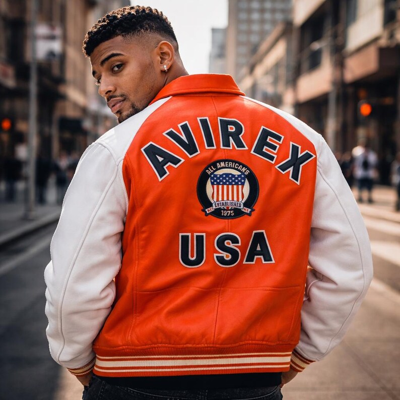 May include: Orange and white varsity jacket with the word "AVIREX" arched across the top and "USA" at the bottom. The jacket features a circular emblem with the American flag and the words "ALL AMERICANS ESTABLISHED 1975".